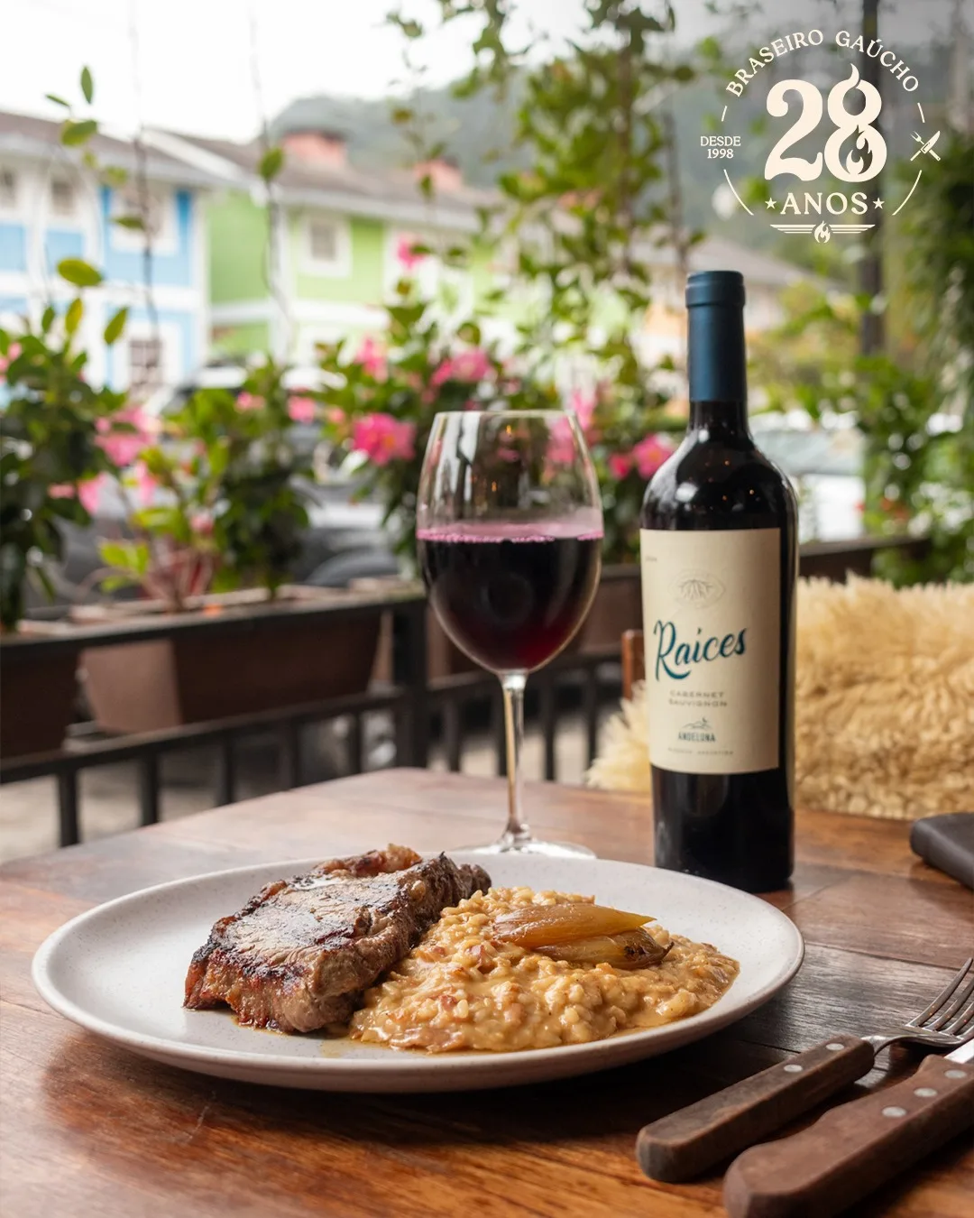 Prato de bife com risoto, taça e garrafa de vinho na varanda florida